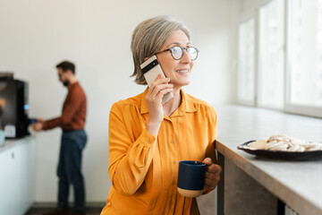 Successful smiling senior woman holding mobile phone and coffee cup