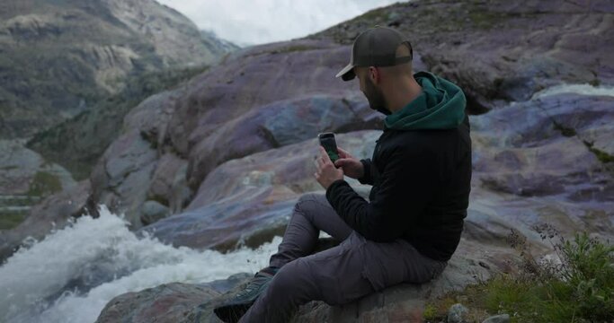 Male tourist takes smartphone pictures on mountain waterfall
