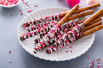 Chocolate dipped pretzel rods with pink heart sprinkles on a plate - obrazy, fototapety, plakaty