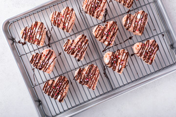 Pink heart shaped rice krispie treats drizzled with dark chocolate on a cooling rack