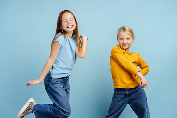 Portrait of smiling girls, cute sisters dancing, having fun isolated on blue background. Childhood,...