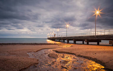 A jetty with lights at dawn reflecting light onto a stream flowing across the beach sand at Mission...