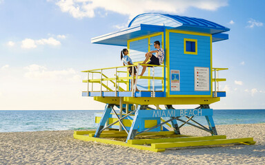 Miami Beach, a couple on the beach in Miami Florida, lifeguard hut Miami Asian women and caucasian men on the beach during sunset. man and woman relaxing at a lifeguard hut looking at a blue ocean