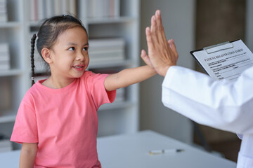 A female doctor stands and holds a file of a young patient's medical history. She uses her hand to...