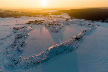 Flooded V-shaped sand pit covered with snow, aerial view of snowy landscape