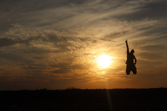 Man pointing his finger towards sky with folded legs and jumping during sunset