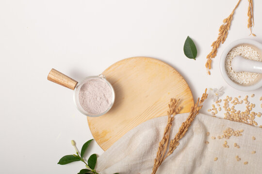 Whole rice, rice bran powder and props are arranged on a white background. Rice Bran powder contains 10% phytic acid, which gently exfoliates the skin and controls skin pigmentation.