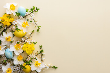 Festive background with spring flowers and Easter eggs, white daffodils and cherry blossom branches on a yellow pastel background