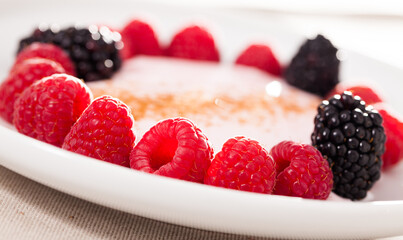 Raspberries and blackberries laid out on a white plate in circle with yogurt and cinnamon