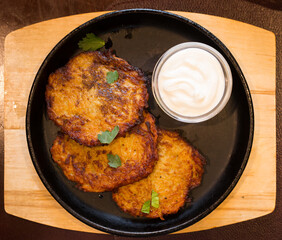 Potato pancakes with sour cream on frying pan. top of view