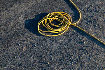 Heavy gage yellow electrical extension cord running over an asphalt street
 - obrazy, fototapety, plakaty