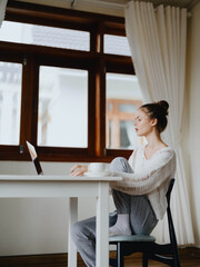 Creative young woman working at a desk at home in a cozy interior with a cup of drink, home office freelancer with a smile, communication and education online