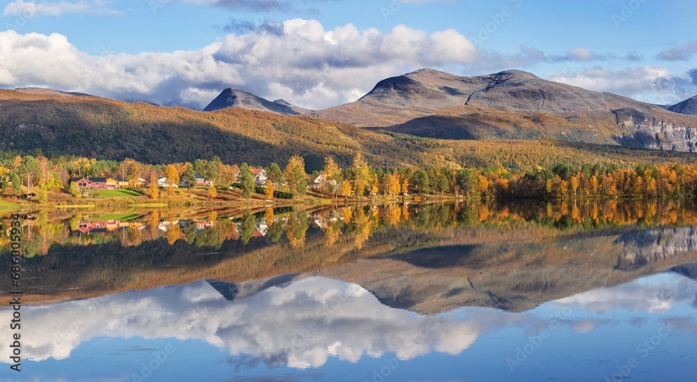 Wall mural beautiful scenic landscape with mountain and autumnal forest under the sky reflecting in surface of water in Norway.