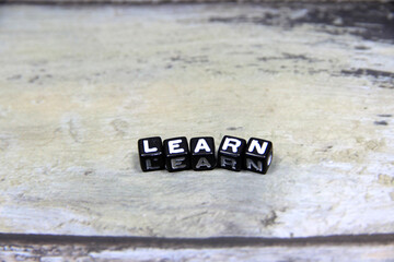 "LEARN" text or message short word letter on black plastic block with wood pantern background.Copy space.