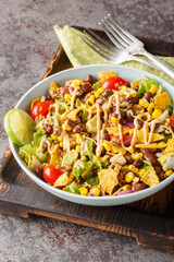 Taco salad is a warm salad made with chili beans, spicy ground beef, corn, lettuce, cheese and avocado closeup on the plate on the table. Vertical