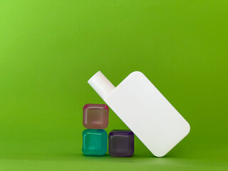 Still life of white cosmetic jar and coloured ice cubes on green background