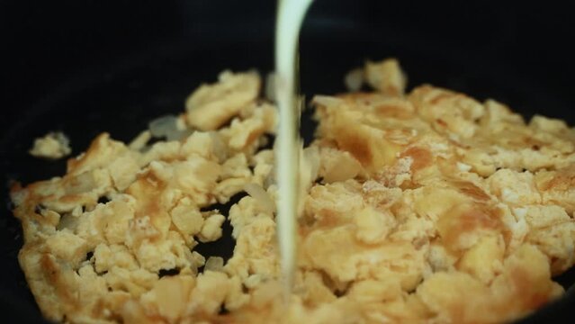 A time lapse close up shot, turning over the omlet on a black hot pan and scrumbling the eggs, making a breakfast 4K video