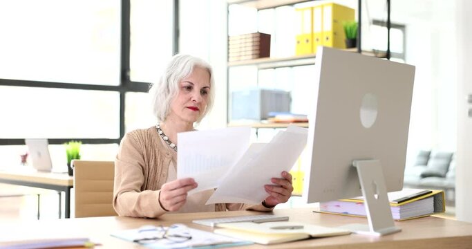 Elderly businesswoman studying documents at her desk in office 4k movie slow motion. Bureaucracy and paperwork concept