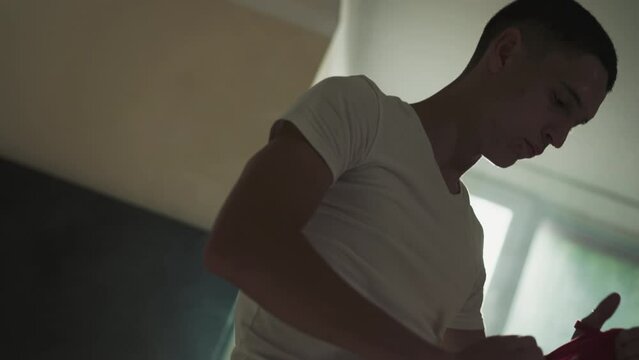 Fighter uses hand wrap for boxing in combat gym. Concentrated athlete applies protective supply for palms in martial arts club slow motion. Sportive life