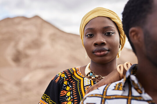 Fashion portrait of African American couple wearing traditional clothing and posing in desert, focus on woman looking at camera