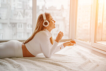 Side view portrait of relaxed woman listening to music with headphones lying on carpet at home. She...