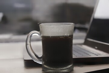 Laptop with cup of black coffee and glass.
