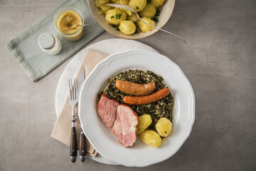 Oldenburger Grünkohl mit geräucherter Kohlwurst, Pinkel, Kassler Nacken, Kartoffeln, Senf, Petersilie auf Teller und hell grau Stein Hintergrund