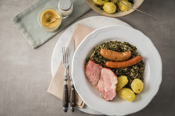 Oldenburger Grünkohl mit geräucherter Kohlwurst, Pinkel, Kassler Nacken, Kartoffeln, Senf, Petersilie auf Teller und hell grau Stein Hintergrund