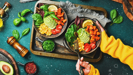 Female hands holding Buddha Bowl: lunch of avocado, pumpkin, cherry tomatoes, corn and lettuce. Diet. Healthy balanced eating. - obrazy, fototapety, plakaty