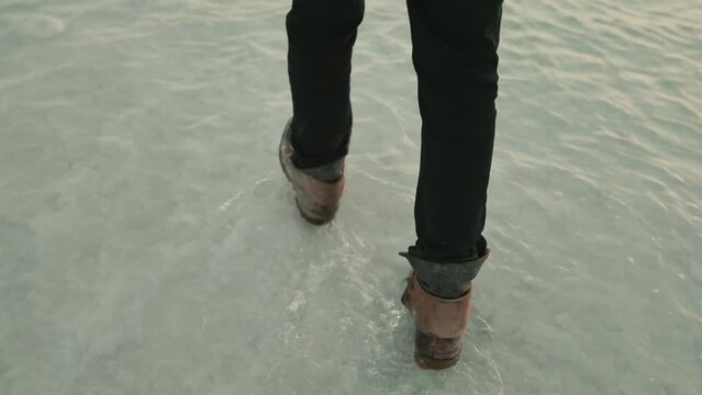 Follow cam of man wearing jeans and leather boots walking in ankle deep water