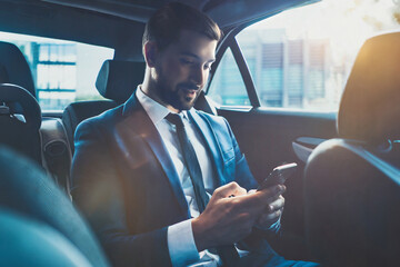 Busy working day. Handsome young man in full suit looking at his smart phone and sitting in the luxury car.Young perfectionist businessman concentrate on the phone.Close-up. - Powered by Adobe