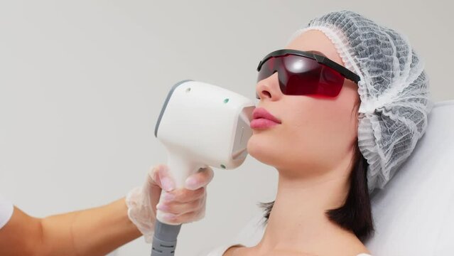 Therapist-cosmetologist performs laser treatment on a woman's face in a beauty spa clinic. Close-up. The concept of advertising healthy and clean facial skin.