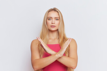 Serious blonde woman in pink top stands looking straight at camera with her arms crossed at chest in prohibitory sign, warning concept, copy space