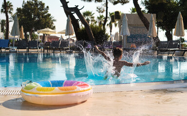 A child leaps into the pool, water erupting around; shot from the side. Captures the carefree...
