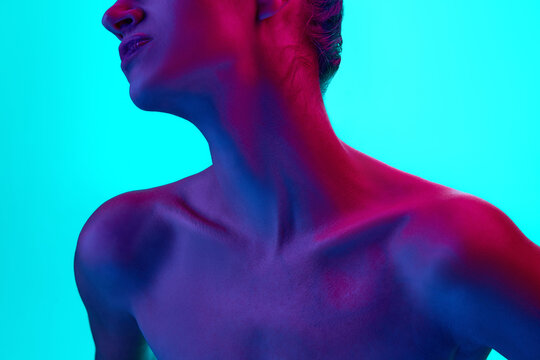 Cropped image of female neck and collarbones against blue background in neon light. Model posing naked. Body aesthetics, beauty