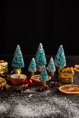 Top view of Christmas decoration with trees, candle, snow and orange on wooden table, black background, vertical, with copy space
