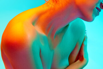 Cropped image of naked female body, woman sitting and covering breast with hand against blue...