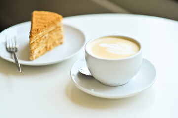 a cup of cappuccino latte with latte art and cake on the table.