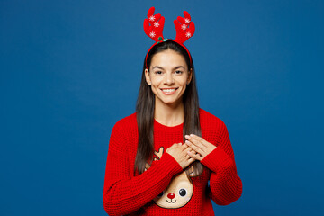 Merry thankful grateful young Latin woman in red Christmas sweater fun decorative deer horns on...