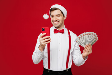 Merry young man in white shirt Santa hat posing hold fan of cash money in dollar banknotes use...
