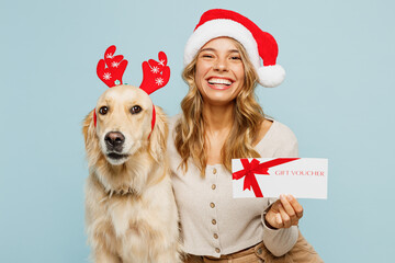 Young happy owner woman with wears casual clothes Santa hat hug best friend retriever dog hold store gift certificate coupon voucher card isolated on plain blue background. New Year discount concept. - obrazy, fototapety, plakaty