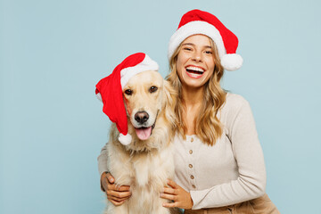 Young smiling owner woman wear casual clothes Santa hat hug cuddle embrace best friend pet retriever dog isolated on plain pastel light blue background studio. New Year Christmas celebration concept.
