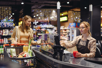 Young customer woman in casual clothes give cashier goods at checkout shopping at supermaket store...