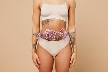 Close up cropped young nice lady woman with slim body perfect skin wear nude top bra lingerie stand with flowers in panties isolated on plain pastel light beige background. Lifestyle diet fit concept. - obrazy, fototapety, plakaty