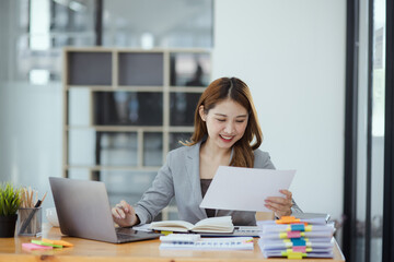 Businesswoman working with stack of documents papers and laptop sitting at office desk.