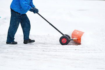 Man removing snow during blizzard. Worker with rolling snow pusher clean snowy sidewalk. Manual...