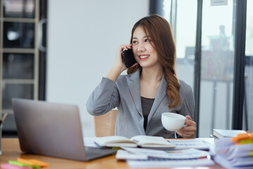 Obraz premium Accounting asian woman use smartphone and laptop at office desk in office, Accounting businesswoman online working concept.