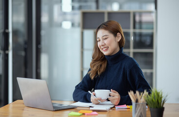 Happy young asian businesswoman with laptop sitting at workplace in modern office.