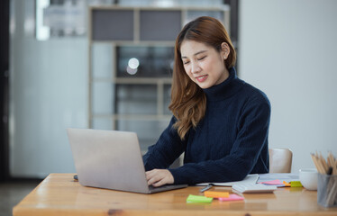 Fototapeta na wymiar Happy young asian businesswoman with laptop sitting at workplace in modern office.