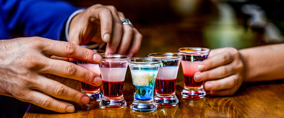 Man hands glasses of shot or liqueur. Glasses of alcohol. Tequila shots, vodka, whisky, rum. Group friends tequila shot glasses in bar - obrazy, fototapety, plakaty